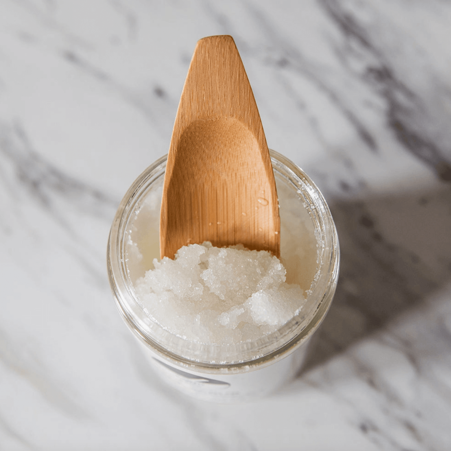 A jar of energizing salt scrub with a wooden scoop, showcasing the exfoliating texture of Dead Sea salt.