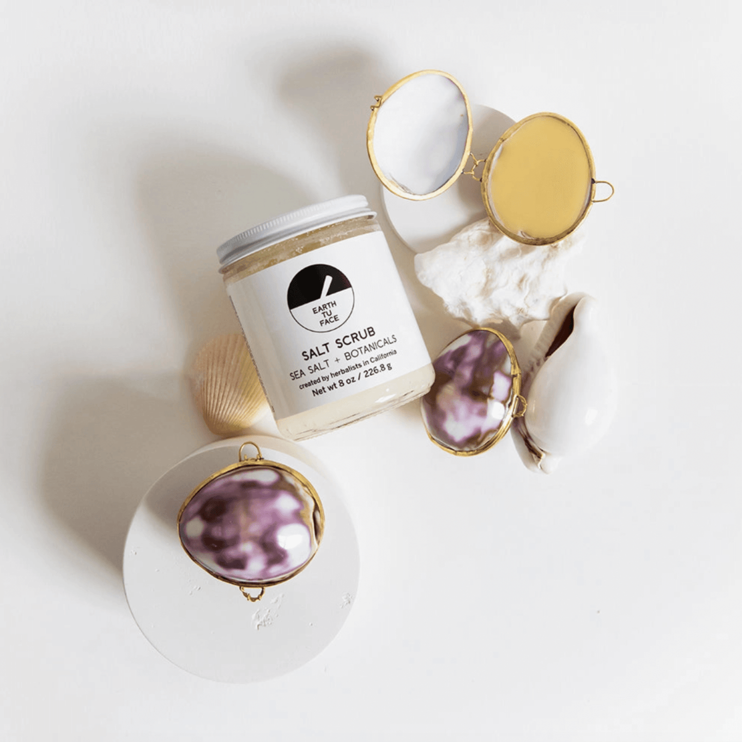 SALT SCRUB jar with seashells and mirrors on a clean white background, highlighting Ayurvedic-inspired skincare.
