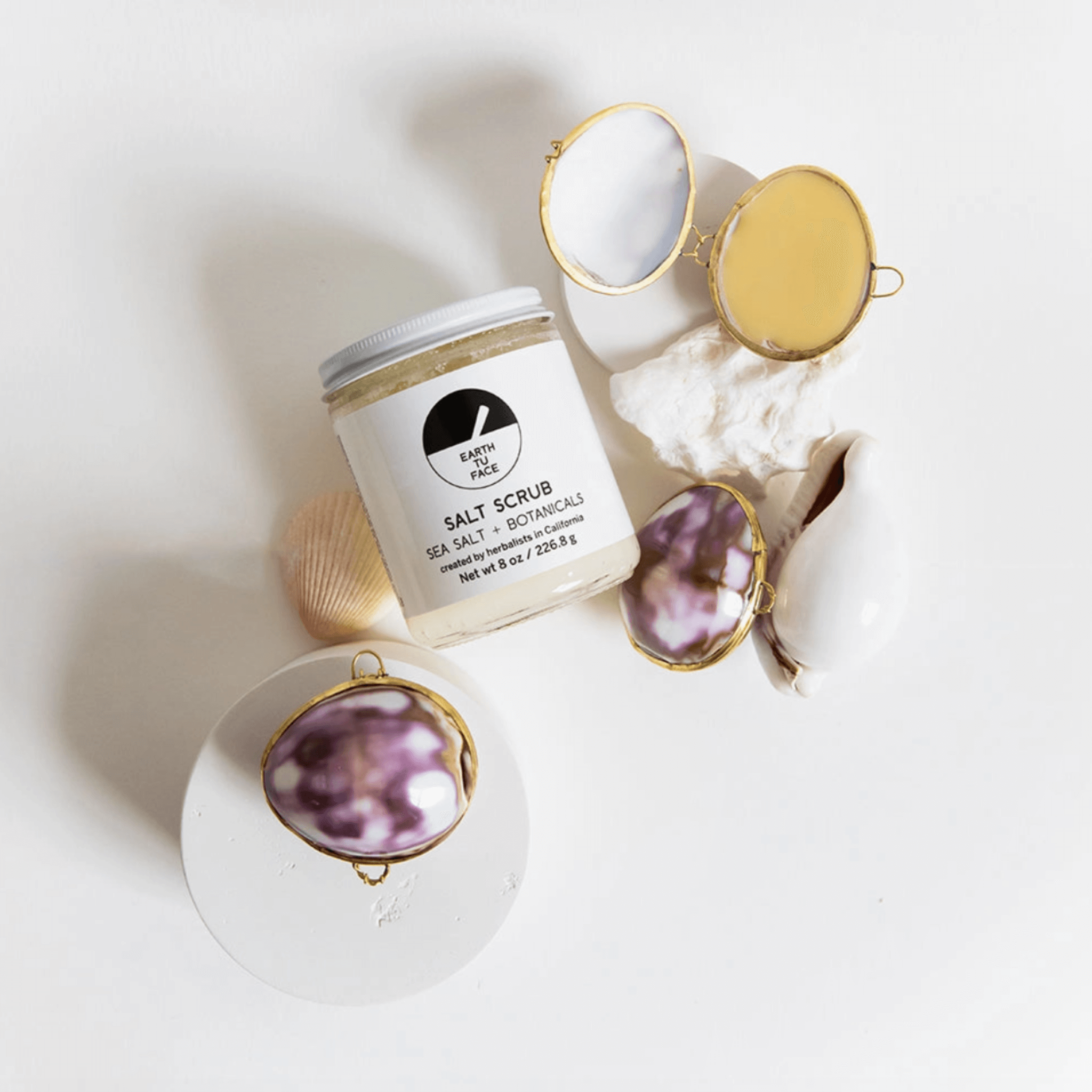 SALT SCRUB jar with seashells and mirrors on a clean white background, highlighting Ayurvedic-inspired skincare.