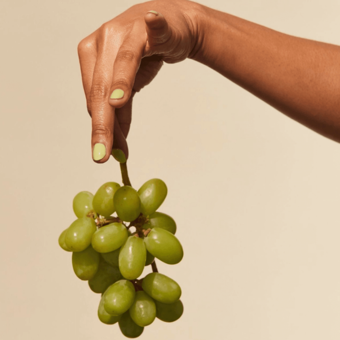 Hand holding a bunch of green grapes, showcasing playful light green Veggie nail polish.