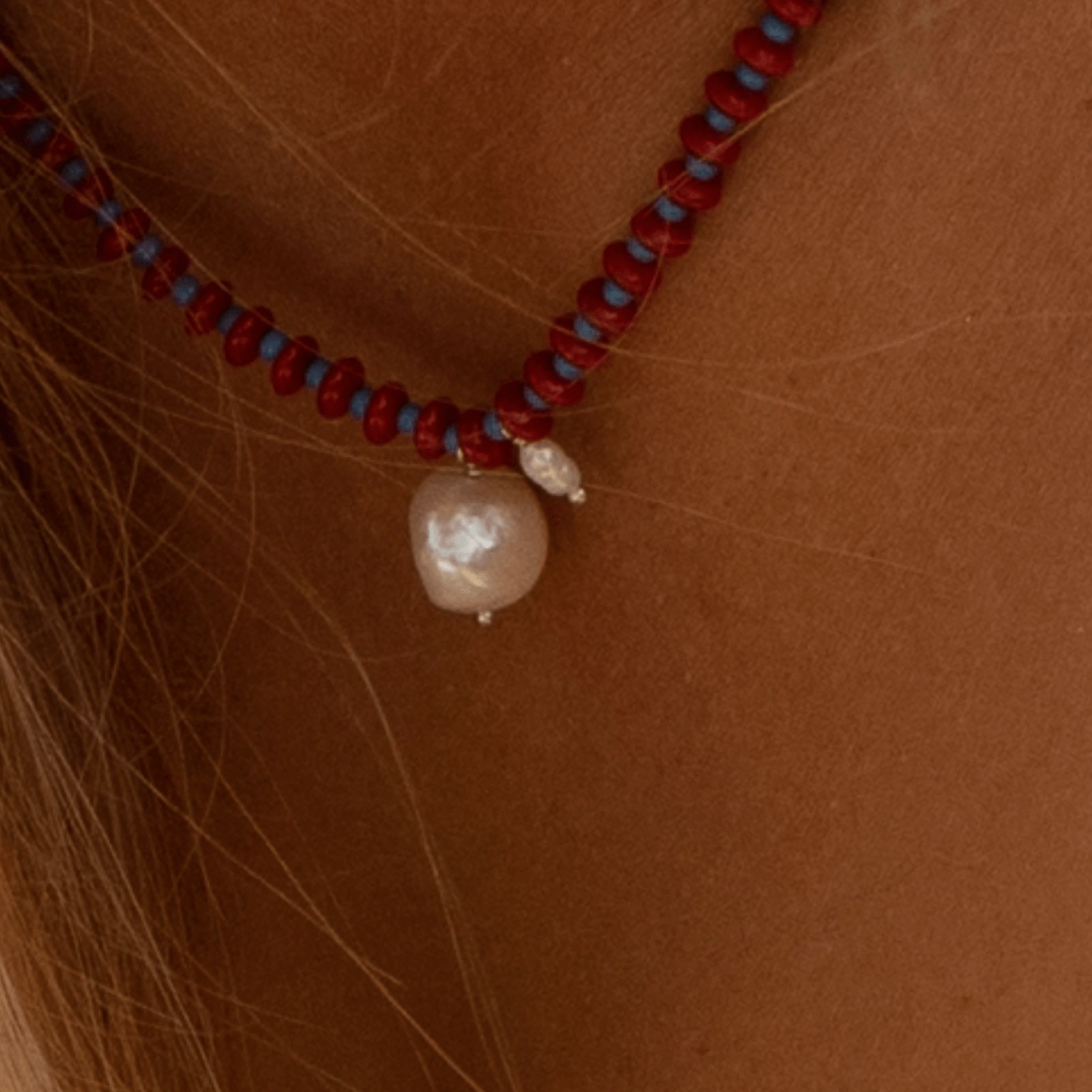 Close-up of Anni Necklace featuring red coral, blue seed beads, and a luminous freshwater pearl accent.