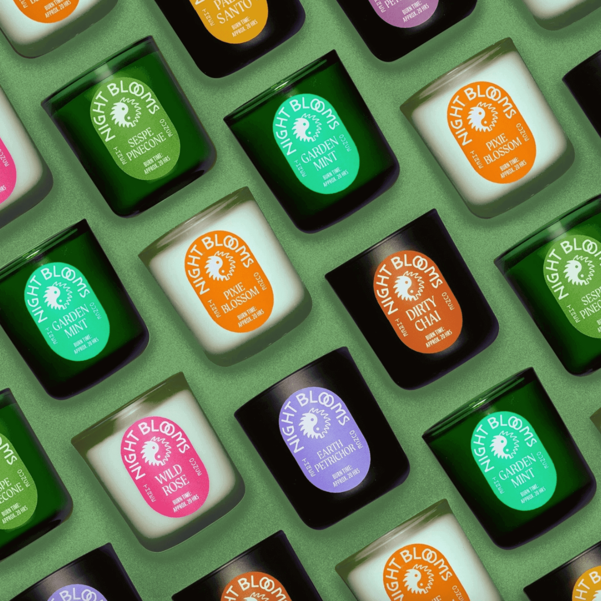 Colorful collection of Night Blooms candles in various scents, showcasing their stylish labels on a green background.