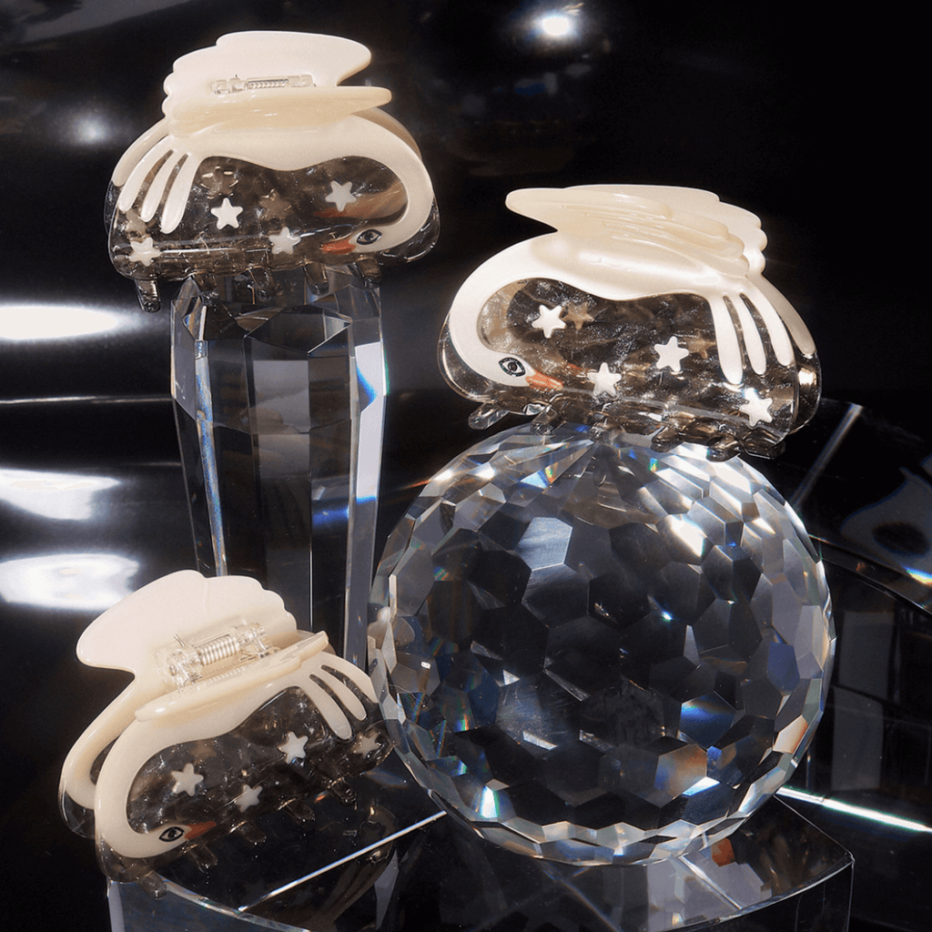 CYGNUS SWAN + STARS HAIR CLAW showcased on crystal display, featuring celestial swan design and shimmering colors.