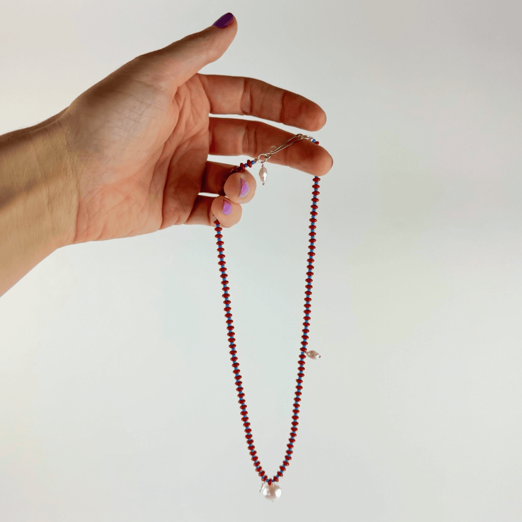 Hand holding Anni Necklace featuring red coral, blue seed beads, and pearls, showcasing its elegant design and craftsmanship.