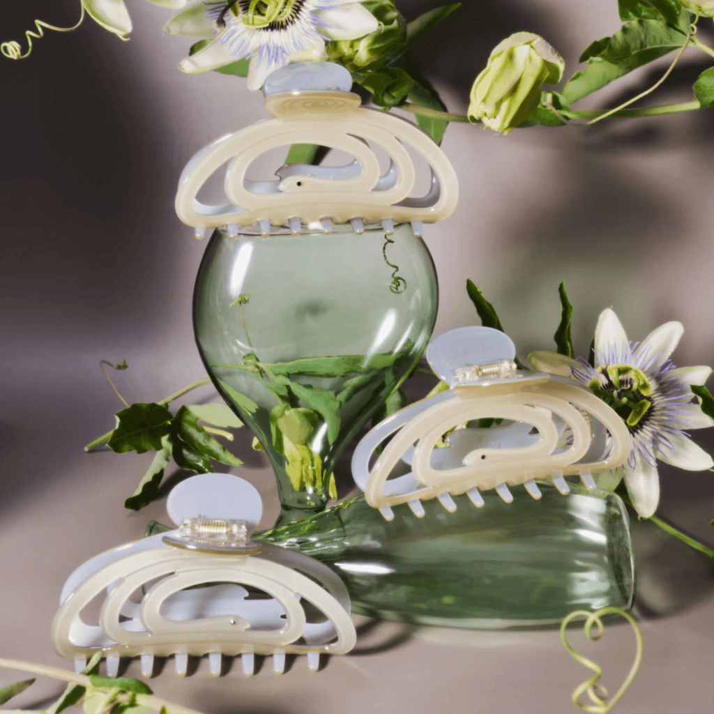 Three CORRA HAIR CLAW clips elegantly displayed on green glass, showcasing their shimmering pale green design.