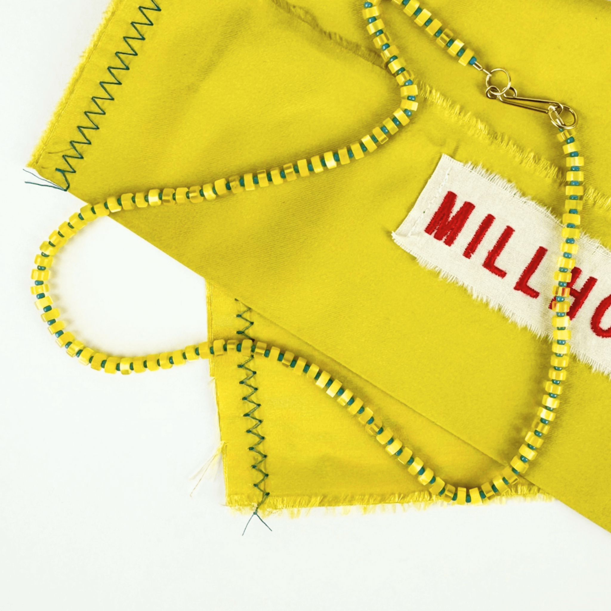 Galileo Necklace featuring colorful optic glass beads on a vibrant yellow fabric background.