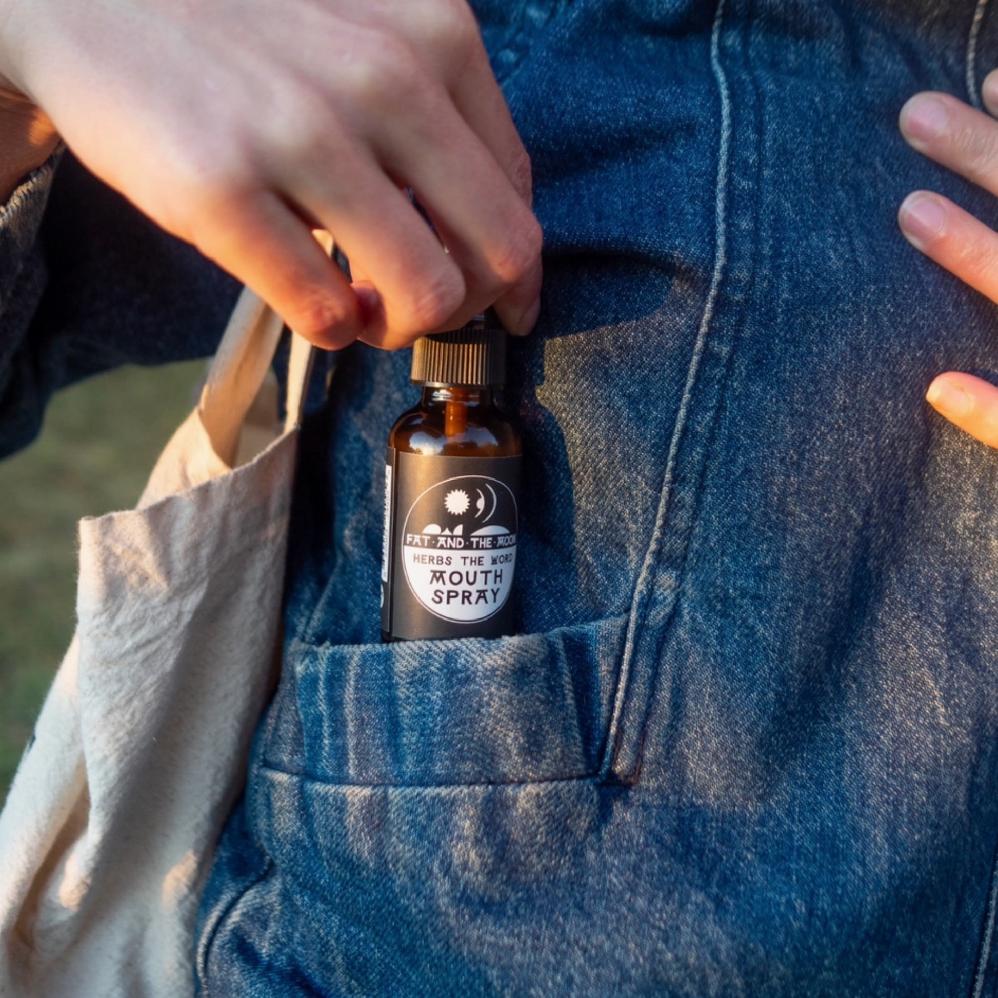 Person holding a bottle of Herbs the Word Mouth Spray nestled in a denim pocket, ready for fresh breath anytime.