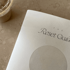 The Reset Guide workbook next to a refreshing drink, perfect for self-discovery and intentional living.