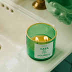 Green CASA POLANCO candle with golden rim glowing softly, evoking elegance and tranquility in a chic bathroom setting.