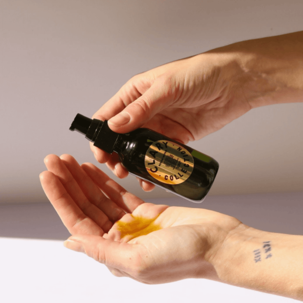 Hands dispensing RENEW + REPAIR OIL, a restorative body oil in a dark glass bottle for skin healing and hydration.
