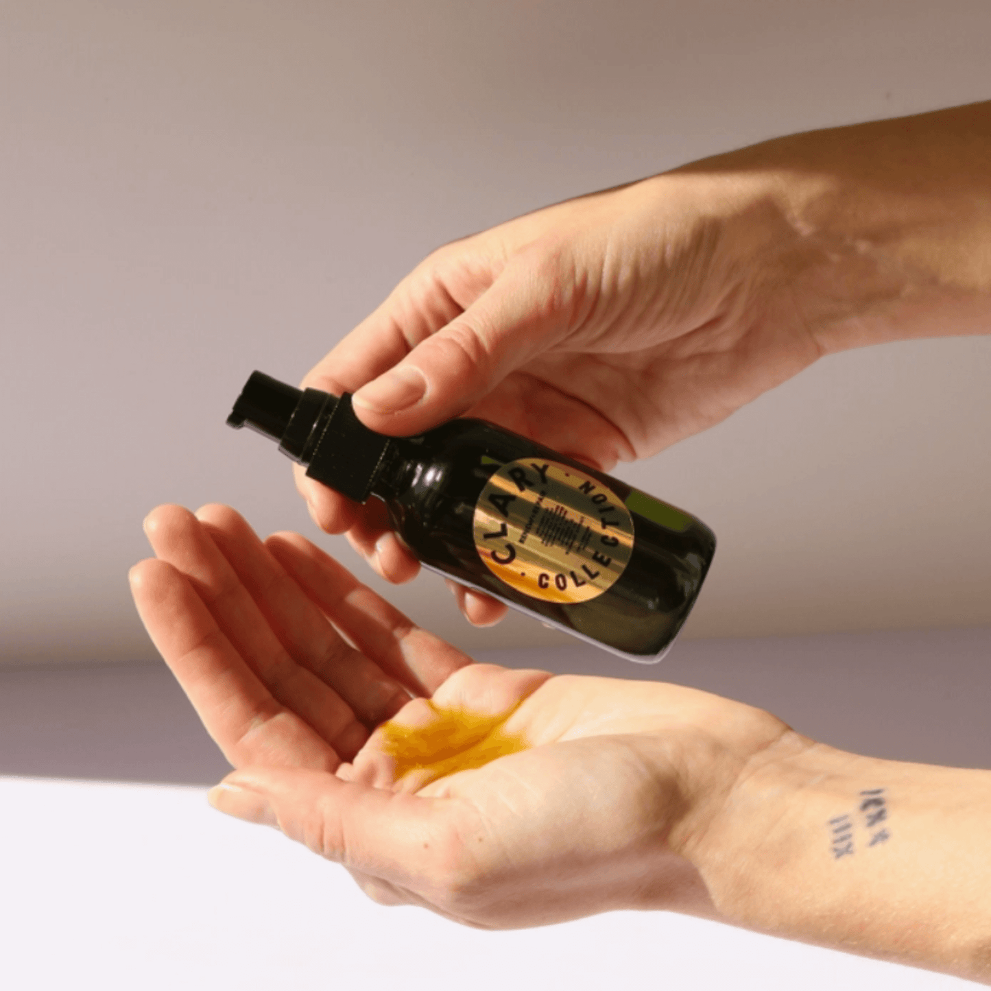 Hands dispensing RENEW + REPAIR OIL, a restorative body oil in a dark glass bottle for skin healing and hydration.