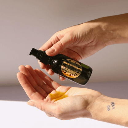 Hands dispensing RENEW + REPAIR OIL, a restorative body oil in a dark glass bottle for skin healing and hydration.