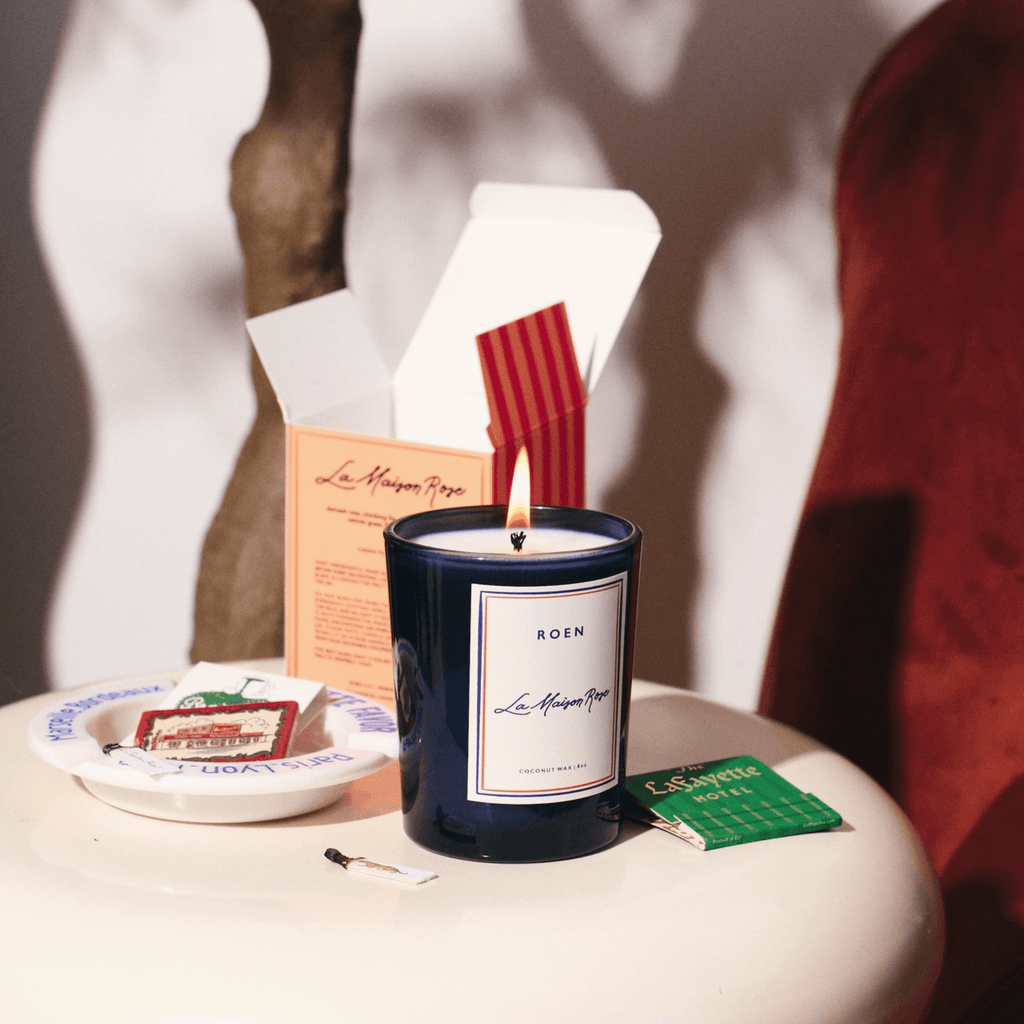Elegant LA MAISON ROSE candle in a stylish navy jar, radiating warmth with a flickering flame on a chic table.