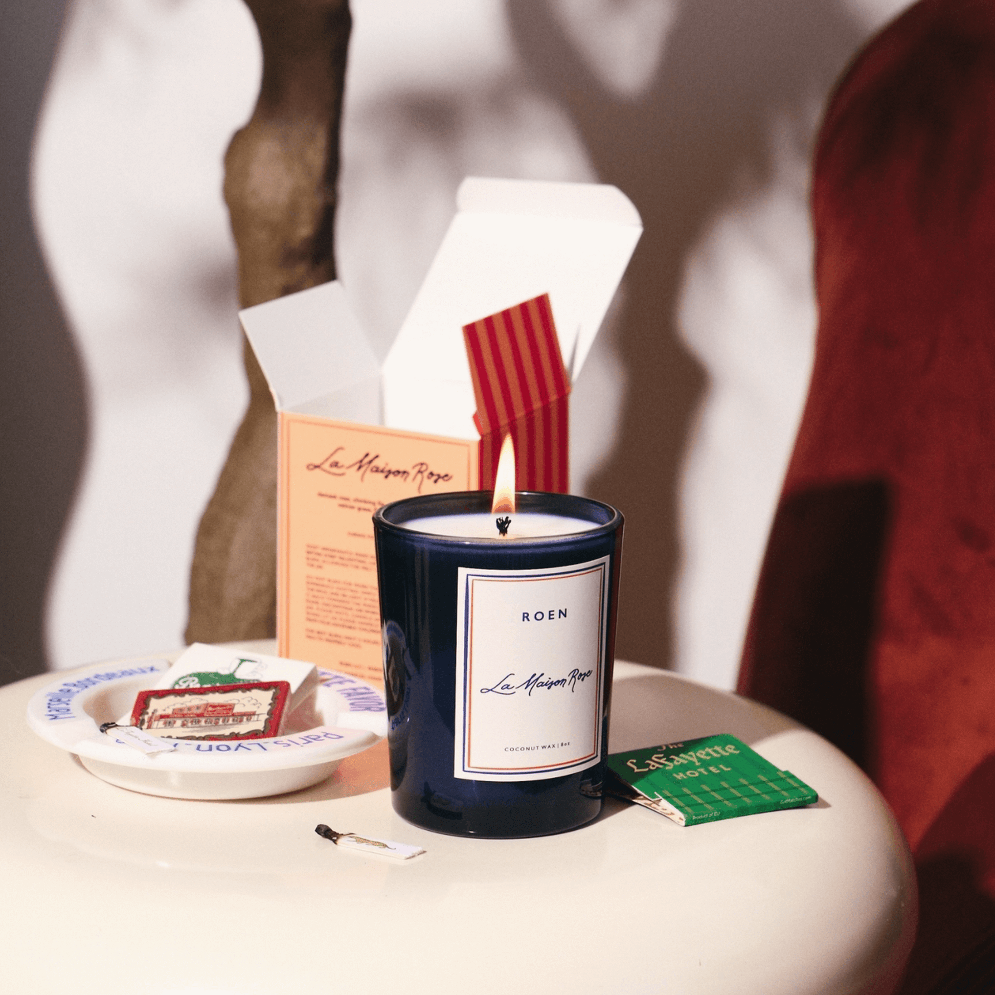 Elegant LA MAISON ROSE candle in a stylish navy jar, radiating warmth with a flickering flame on a chic table.