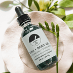 2 oz bottle of Earth Face Bath and Body Oil with blue chamomile and sandalwood, surrounded by natural elements.