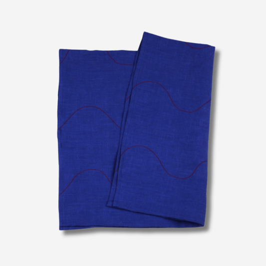 Wavy linen tea towel in vibrant blue with red accents, featuring stitched details and a hanging loop.