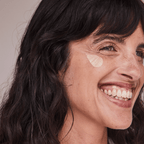 Woman applying Essential Tinted SPF 30, showcasing radiant skin with sheer coverage and a dewy finish.