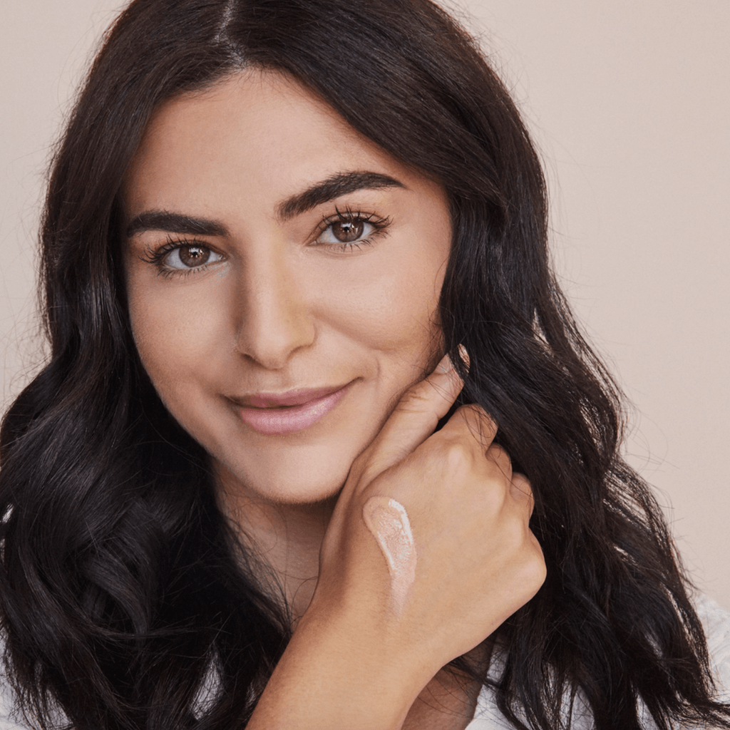 Close-up of a woman showing her hand with a swatch of essential tinted SPF 30, highlighting its sheer coverage and radiant finish.