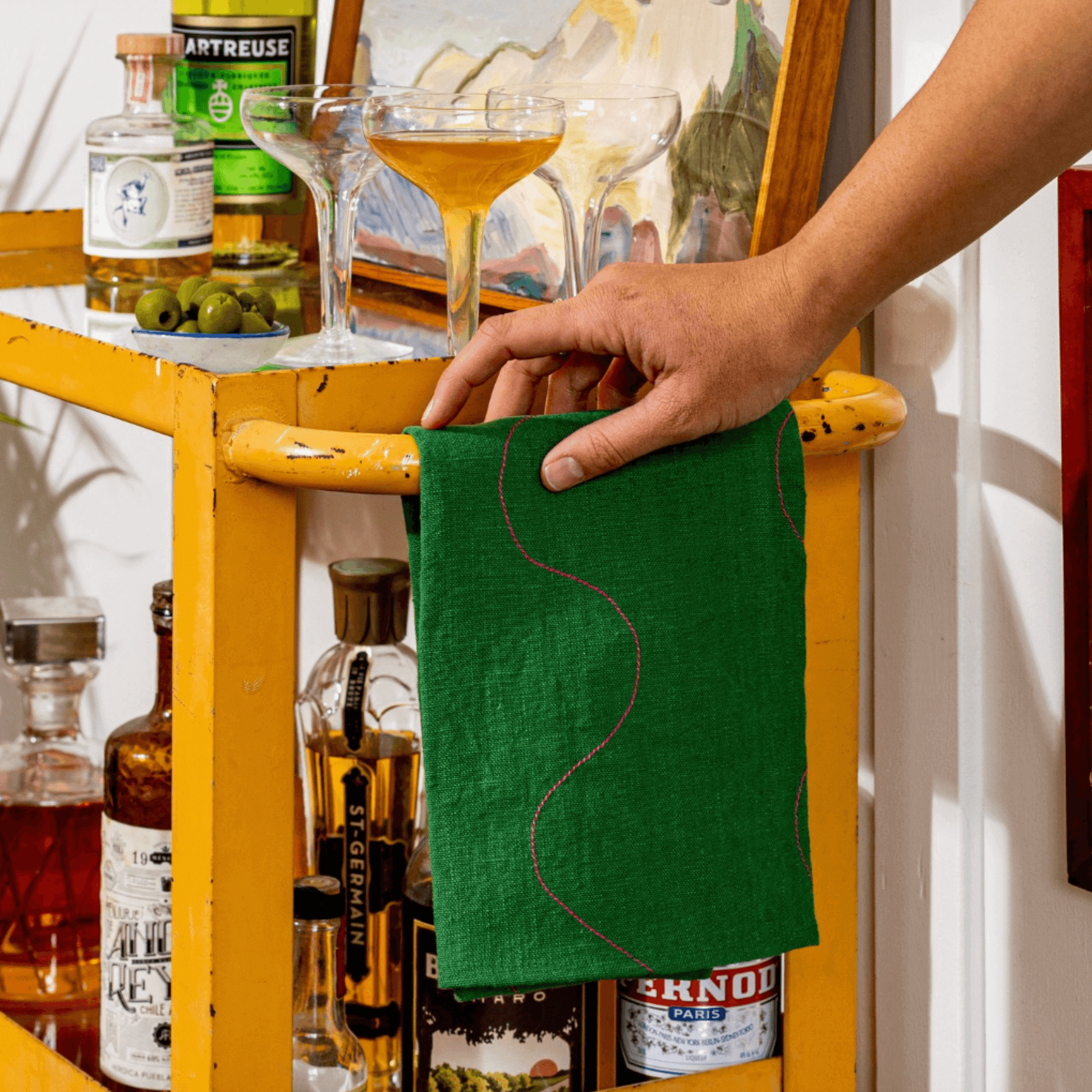 Vibrant green linen tea towel with pink accents hanging on a yellow bar cart, perfect for kitchen decor.