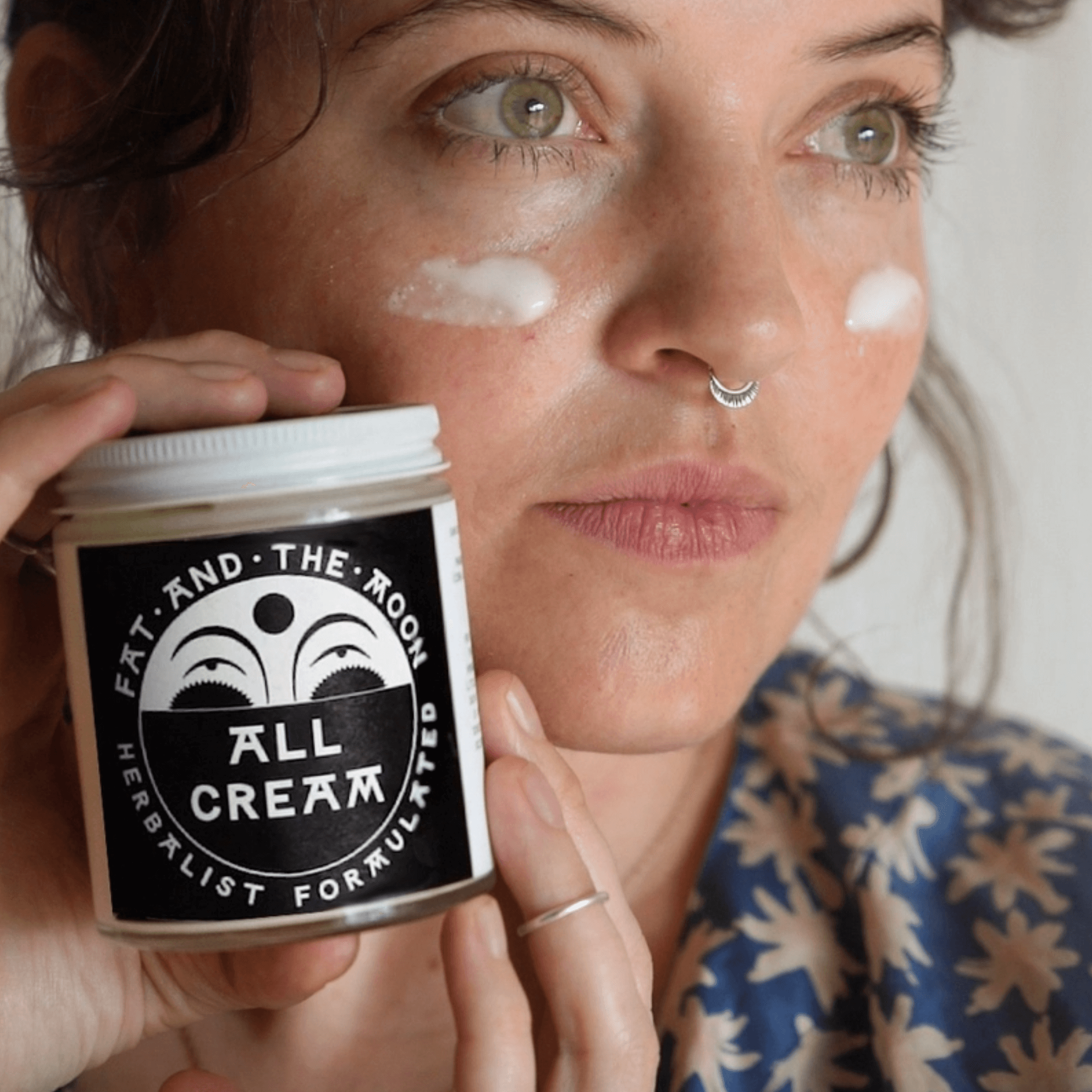 Woman applying Fat and the Moon's All Cream, a herbal face and body moisturizer for hydration and protection.