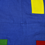 Blue linen apron featuring colorful block corners and contrasting pockets, perfect for kitchen or studio use.