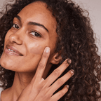 Model applying Kari Gran Essential Tinted SPF 30 on her face, showcasing radiant skin and natural beauty.