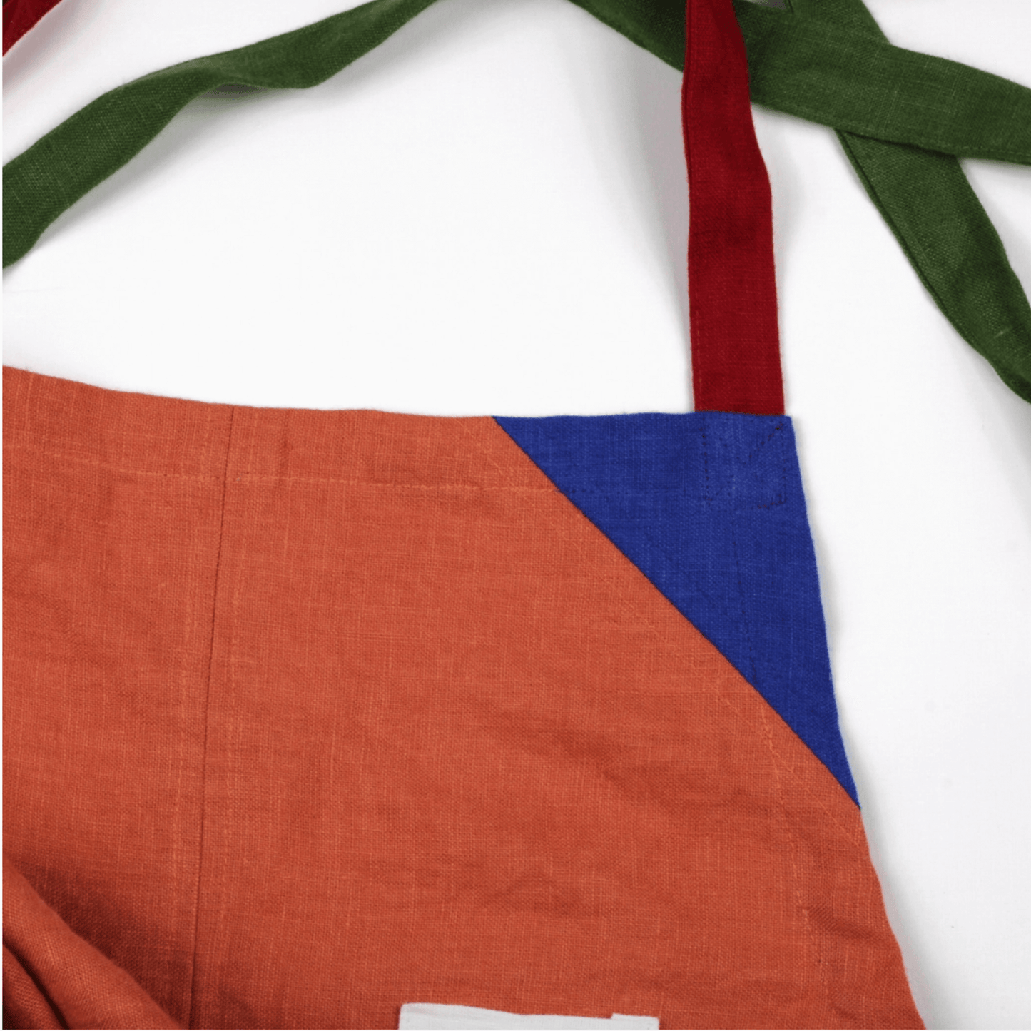 Close-up of an orange linen apron with color-blocked corners and contrasting straps for style and comfort.