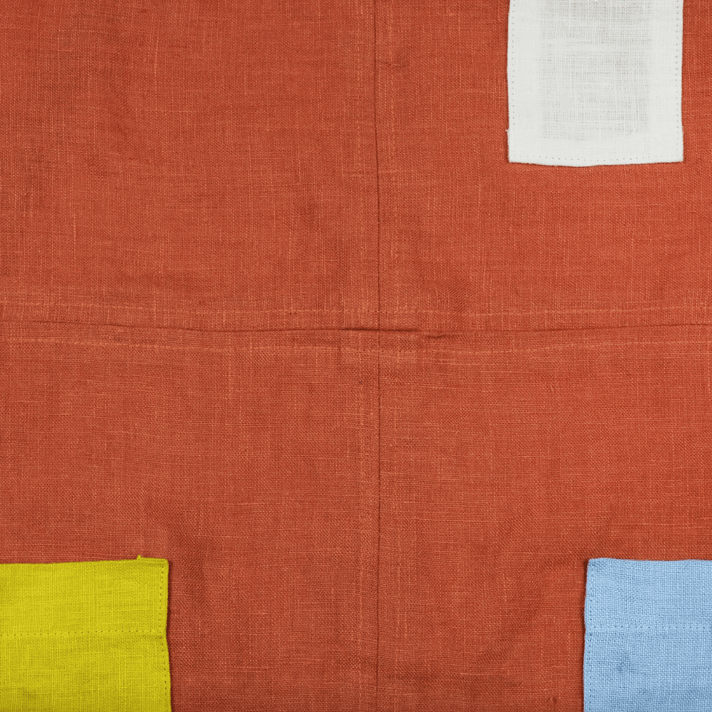 Orange linen apron featuring color-blocked pockets and french-finished seams for durability and style.