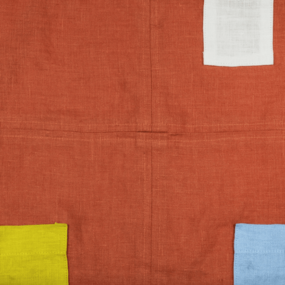 Orange linen apron featuring color-blocked pockets and french-finished seams for durability and style.