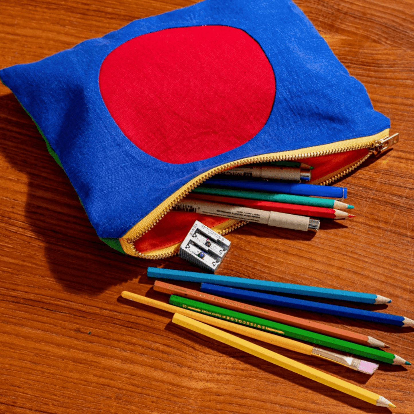 Colorful circle linen zipper pouch with art supplies spilling out on a wooden table.