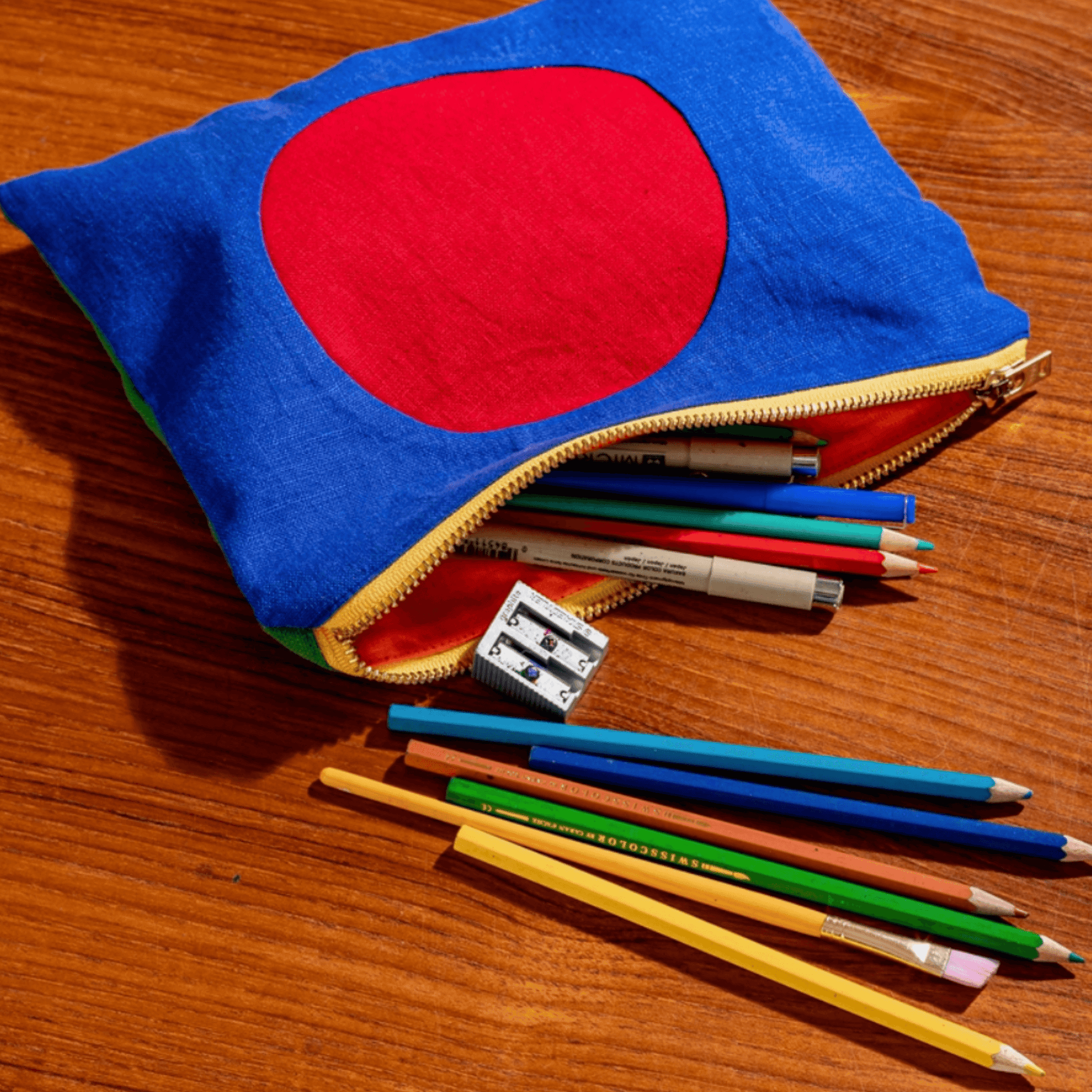 Colorful circle linen zipper pouch with art supplies spilling out on a wooden table.