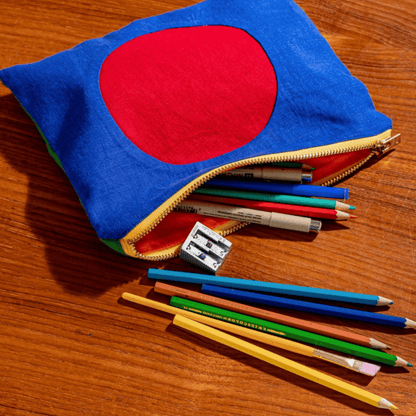 Colorful circle linen zipper pouch with art supplies spilling out on a wooden table.