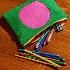 Vibrant CIRCLE LINEN ZIPPER POUCH in green with pink circle, unzipped and filled with colorful pencils on wooden surface.