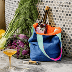 Small linen tote bag in City Slicker design, filled with a wine bottle and fresh produce, showcasing a vibrant, reversible style.