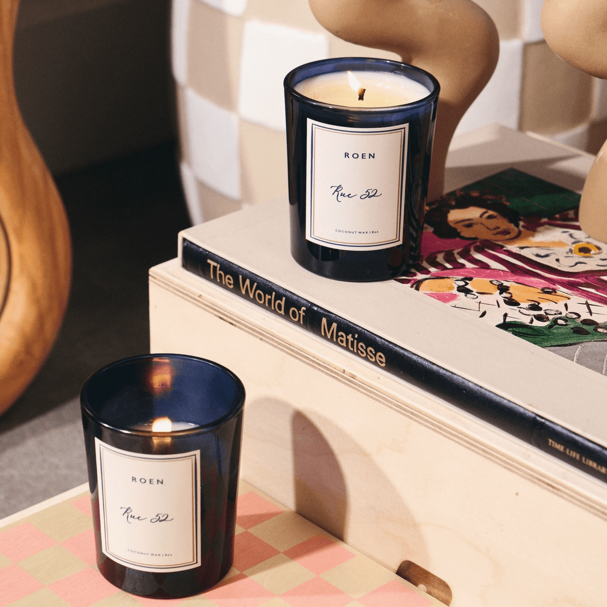 RUE 52 candles on a table beside art books and sculptures, capturing Parisian elegance and rich scents.