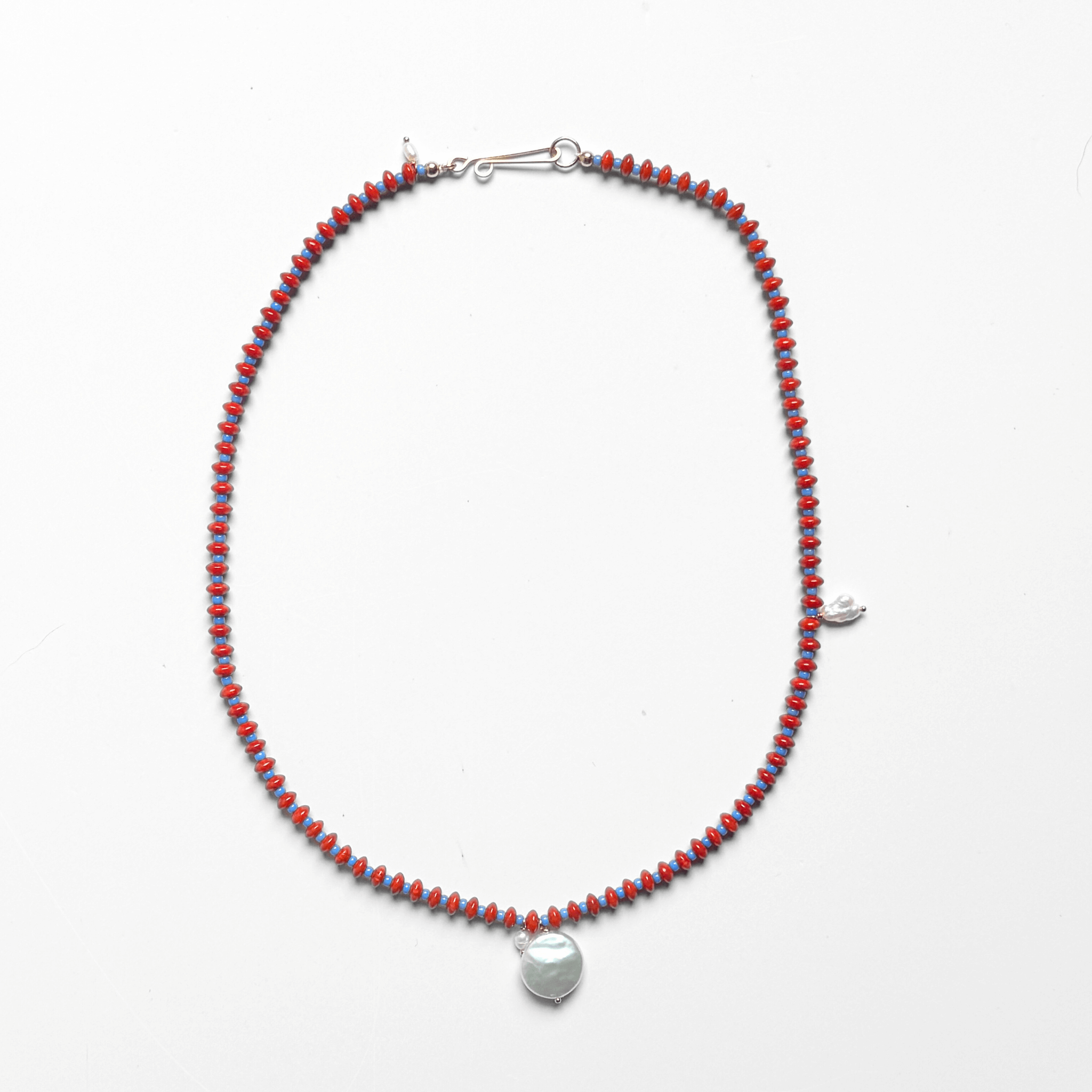 Anni Necklace featuring vibrant red coral, blue seed beads, and a freshwater pearl pendant on silk.