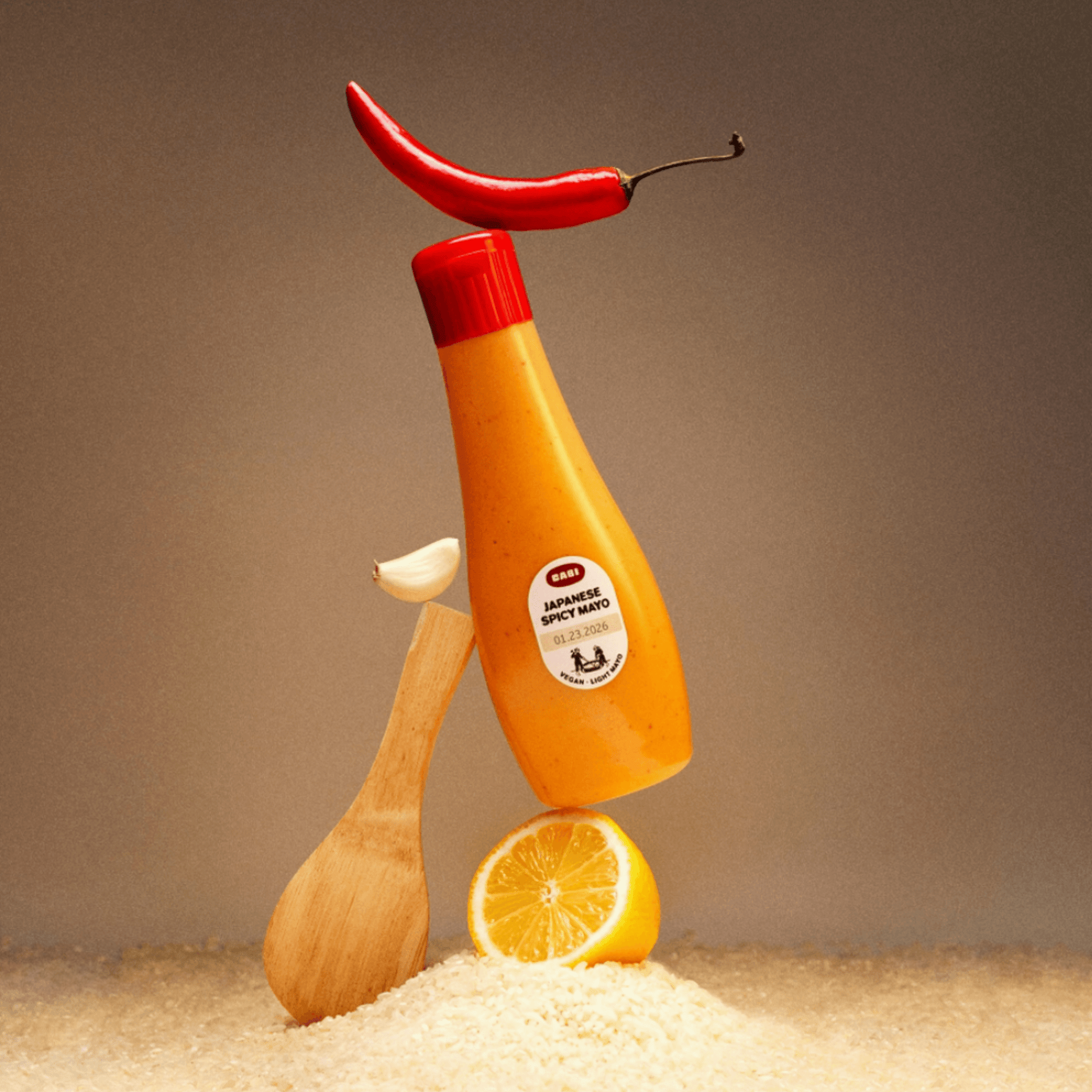 Bottle of Japanese spicy mayo surrounded by rice, lemon, garlic, and a red chili pepper, showcasing vibrant ingredients.