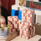 Three beautifully packaged RUE 52 candles with a stylish grid design, sitting on a tabletop surrounded by decor.